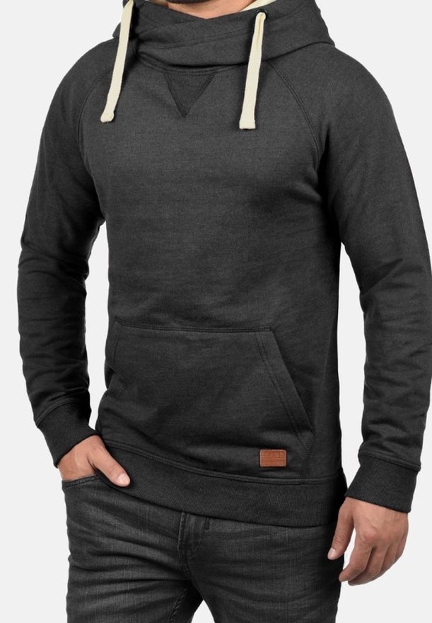 Sudadera gris oscuro con cuello tipo cowl, cordones en crema, bolsillo frontal y un pequeño parche de cuero marrón en el dobladillo. Textura suave, diseño casual.
