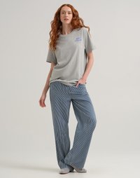 T-shirt di cotone grigio con logo blu "Lee Crayola", abbinato a pantaloni a gamba larga a strisce blu e bianche. Il modello è in piedi con una mano sulla vita.