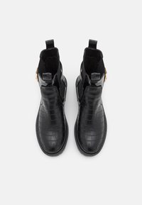 Botas negras hasta el tobillo hechas de un material brillante con patrón de cocodrilo, con punta redondeada, tiradores y un acento lateral en tono dorado.
