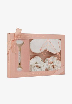 Il set include un rullo facciale in pietra preziosa con una pietra bianca, una mascherina per gli occhi in seta bianca e due scrunchies in seta bianca, il tutto in una scatola rosa.