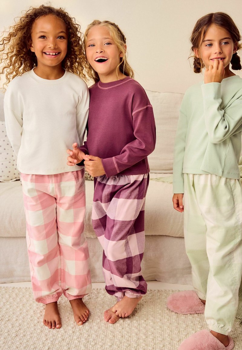 Tre bambini in pigiama: una maglietta bianca con pantaloni a quadri rosa, una maglietta viola con pantaloni a quadri coordinati e una maglietta verde menta con pantaloni chiari.