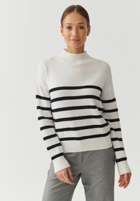 Pull en tricot avec un col montant à côtes, présentant des rayures horizontales noires sur fond blanc. Poignets et ourlet côtelés.