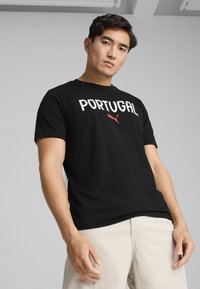 Sort t-shirt lavet af bomuld, med "PORTUGAL" i hvid tekst og et rødt Puma-logo, korte ærmer og rund halsudskæring.