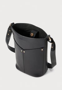 Sac en cuir noir à bandoulière avec sangle ajustable, poche avant avec rivets dorés, et fermeture aimantée, présenté ouvert sur fond blanc.