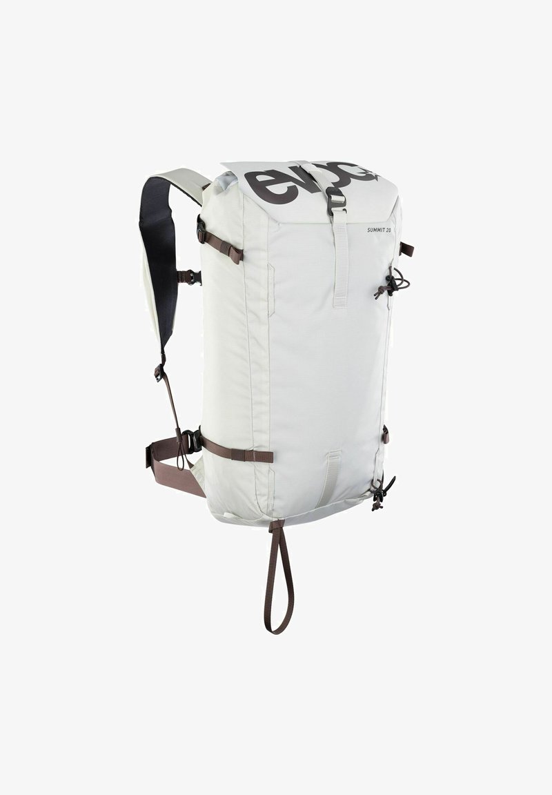 Mochila gris claro con cierre enrollable, correas ajustables marrones y un gran logo negro; cuenta con correas laterales de compresión y un acabado duradero.