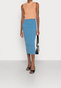 Hedvábný top se zkrácenými rukávy v broskvové barvě a žebrovaná sukně ke kolenům v modré. Černé sandály na podpatku a malá černá kabelka dotvářejí vzhled.