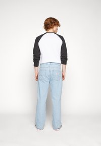 White and black raglan shirt paired with light blue jeans. The shirt has long sleeves, and the jeans feature a back pocket logo patch.