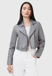 Giubbotto in pelle grigio, corto, stile biker, con chiusure a zip e a bottone, numerose tasche con zip e colletto a punte. Abbinato a una maglietta bianca.