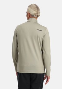 Lichtgrijze lange mouwen shirt gemaakt van gladde stof; is voorzien van een opklapbare kraag en het "SPYDER" logo op de bovenrug.