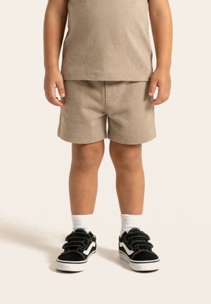 Dijete koje nosi bež kratke hlače i odgovarajuću košulju, bijele čarape i crne tenisice s bijelim potplatima i detaljima.