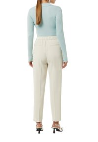 Helles blaues, geripptes Langarmoberteil, cremefarbene tapered Hose mit elastischem Bund und silberne Pumps mit kleinem Blockabsatz.