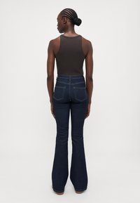 Aukštos juosmens tamsios džinsinės plačios kelnės su užpakalinėmis kišenėmis, derinamos su prigludusia rudą maikę. Lygus paviršius, pritaikytas dizainas.