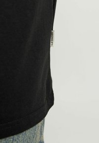 Camiseta de algodón negra con cuello redondo, mangas cortas y una pequeña etiqueta tejida en la costura lateral. Ajuste casual, textura suave.