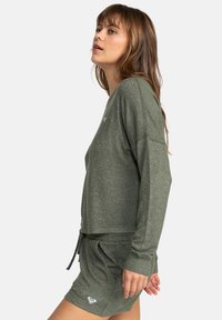 Green heathered long-sleeve top with a loose fit, featuring wide sleeves and a subtle brand logo. Paired with matching shorts.