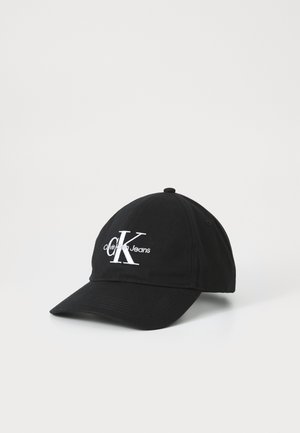 Czarna czapka z daszkiem z białym, haftowanym logo Calvin Klein Jeans na przodzie, prezentowana na jednolitym jasnym tle.