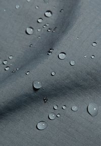 Vanddråber perler på en tekstureret, grå, vandafvisende stofoverflade.