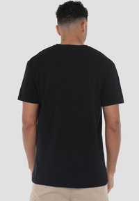 Schwarzes T-Shirt mit kurzen Ärmeln aus Baumwolle. Mit Rundhalsausschnitt und lockerer Passform, mit glatter Textur, von hinten betrachtet.