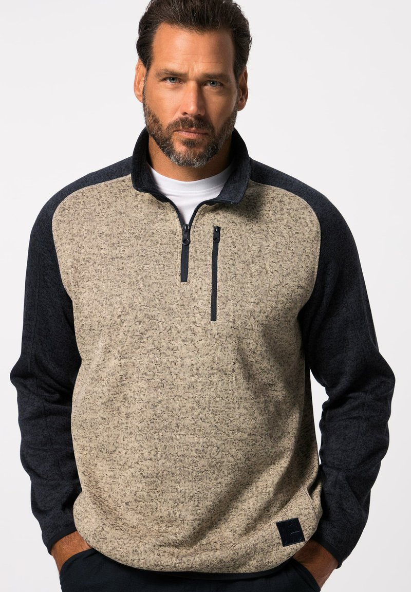Pull en polaire à demi-zip beige avec des manches bleu foncé. Tissu texturé avec une poche poitrine et une étiquette de marque sur l'ourlet. Coupe classique.