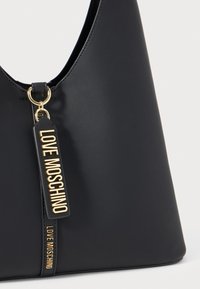 Must mustakangas mustkott mustkott mustkott, millel on kullane metallist "LOVE MOSCHINO" sildike, mis ripub kullast rõngast käepideme lähedal.