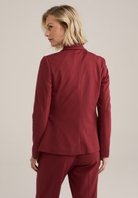 Burgundské prispôsobené sako so slim fit strihom, štruktúrovanými ramenami, hladkým povrchom a jedným rozventom vzadu. Spárované s nohavicami v rovnakom odtieni.