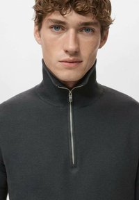 Pull gris foncé à fermeture éclair avec un col montant, tissu texturé et détail de fermeture éclair en métal à l'avant. Coupe ajustée.