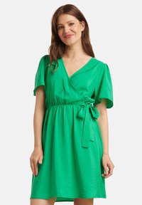 Groene wikkeljurk van textuurstof, met korte mouwen, een V-hals en een strikceintuur in de taille. Eenvoudig en vloeiend ontwerp.