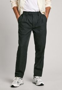 Pelēki uzvalka bikses ar divām priekšējām kabatām, vienu krokotu, jostu ar cilpām un gludu audumu, savienotas ar baltām sporta kurpēm.