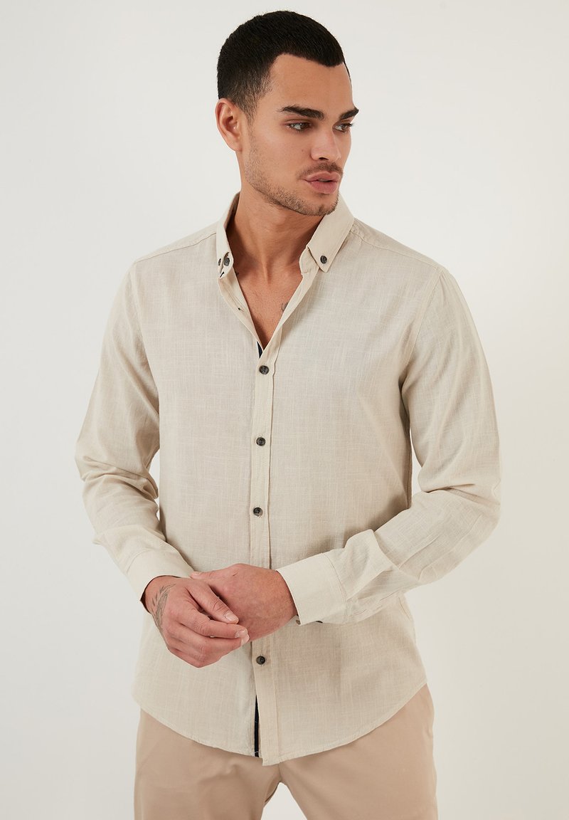 Camisa de manga larga beige en una tela texturizada, con cuello abotonado, parte inferior del cuello en contraste y botones oscuros.