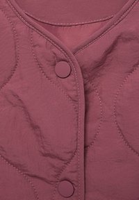 Prošívaná bunda v tlumené mauve barvě, s výstřihem do V, kruhovým šitím a velkými odpovídajícími knoflíky. Hladká, strukturovaná tkanina.