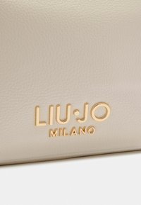 Beige læder handbag med præget guld "LIU·JO MILANO" logo, glat tekstur og rene linjer. Rent og moderne design.