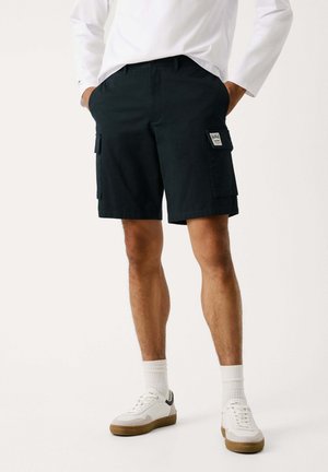 Pantaloni cargo in un blu scuro, realizzati in misto cotone, con tasche laterali, un'etichetta e una vestibilità rilassata. Abbinati a sneaker bianche.
