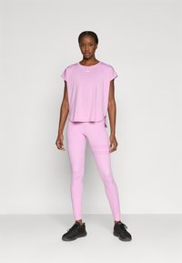 Αθλητικό τοπ σε ανοιχτό ροζ με κοντά μανίκια, σετ με εφαρμοστά κολάν με διακριτικές οριζόντιες ρίγες, συνδυασμένο με μαύρα αθλητικά παπούτσια.