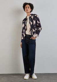 Camicia a maniche lunghe in nero e pesca con motivo geometrico, abbinata a jeans dritti blu scuro e sneaker bianche. Tessuto testurizzato, vestibilità casual.