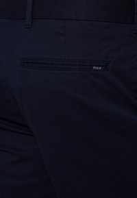 Laivastonsiniset puuvillahousut, joissa on tasainen takatasku, jossa on hillitty "Polo"-merkki. Sileä kangas ja muotoiltu design tarjoavat rakenteellisen istuvuuden.