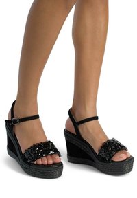 Sandali wedge neri con una base strutturata, decorati con una fascia di perline e una cinghia alla caviglia con fibbia. Design open toe che mette in mostra i piedi nudi.