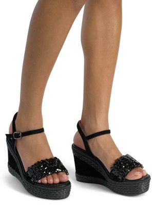 Sandali wedge neri con una base strutturata, decorati con una fascia di perline e una cinghia alla caviglia con fibbia. Design open toe che mette in mostra i piedi nudi.
