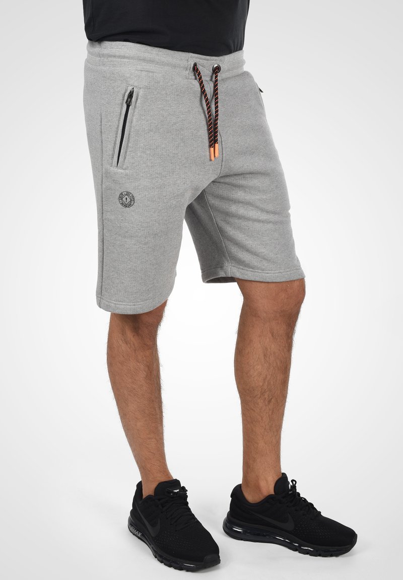 Grijze korte broek met een textuurafwerking, ritssluiting zijzakken en een trekkoord met zwarte en oranje accenten. Logo-opdruk op de dij.
