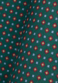 Zielona tkanina z powtarzającym się geometrycznym wzorem czerwonych kwadratów z żółtymi środkami i niebieskimi kwiatami, tworząca teksturowany motyw.