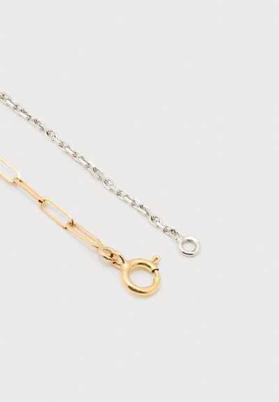 Χρυσή και ασημένια αλυσίδα. Το χρυσό τμήμα είναι επιμηκυμένο και συνδεδεμένο, ενώ το ασημένιο τμήμα είναι μικρότερο και στρογγυλό με κούμπωμα.