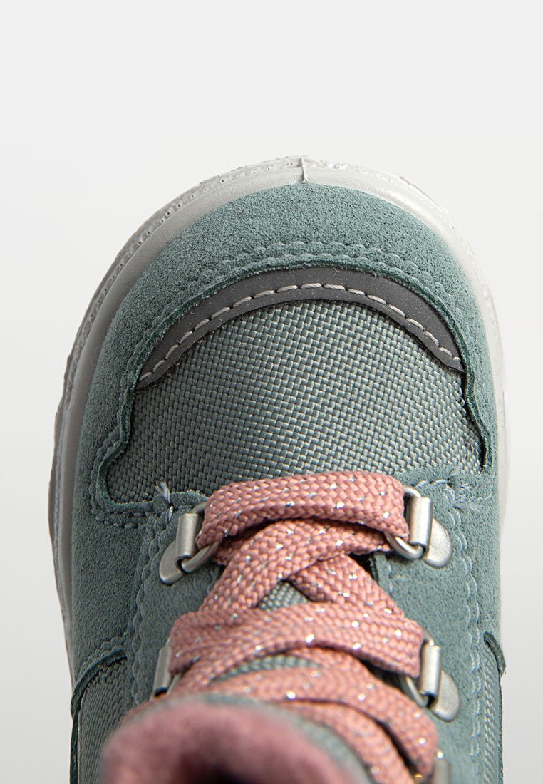 Grüne Wildleder- und Textil-Schuhe mit rosa Glitzer-Schnürsenkeln, silbernen Ösen und weißer Gummisohle. Sie verfügen über ein abgerundetes Design der Zehenpartie.