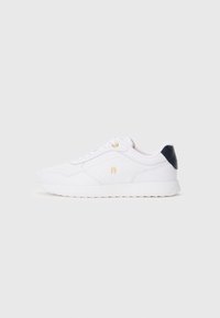 Λευκό χαμηλό sneaker με χρυσά μάτια και λεπτομέρειες λογότυπου, ναυτικό μπλε πίσω τμήμα και λευκή σόλα, εμφανιζόμενο από την εξωτερική πλευρά σε ουδέτερο φόντο.
