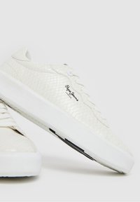 Bílé texturované nízké tenisky s tlustou podrážkou a černým logem "Pepe Jeans London" na straně, zobrazené na jednobarevném světlém pozadí.