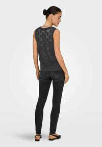 Top senza maniche in pizzo grigio con orlo a scallop, abbinato a jeans skinny scuri. La modella indossa sandali neri. Vista posteriore.
