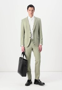 Hele roheline ülikond kahe nööbiga, koos valge särgiga. Sile kangas, slim-fit disain. Must nahast käekott ja kingad.