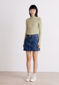Svijetlozeleni rebrasti rolak, plava traper suknja i bijeli visoki tenisice. Outfit ima prilagođen siluetu i minimalne detalje.