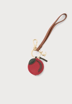 Portachiavi con pochette rossa testurizzata a forma di frutta, dettaglio di foglia verde, anelli in metallo dorato e cinturino da polso in pelle marrone su sfondo bianco.