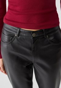 Černé kožené kalhoty s hladkou texturou, se dvěma předními kapsami, zapínáním na knoflík a jemnými detaily šití.