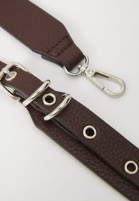 Cinghia in finta pelle marrone con texture e hardware in metallo argentato. Presenta anelli in metallo e un moschettone per il fissaggio.