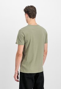 Olivegrünes Baumwoll-T-Shirt mit Rundhalsausschnitt, kurzen Ärmeln und geradem Saum. Auffälliges Detail ist ein kleines Logo auf dem Ärmel.