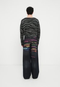 Υπερμεγέθη σκούρα τζιν από τζιν με πολύχρωμα κείμενα και γκρι πουλόβερ με ρίγες ζέβρας, με χαλαρή, υφασματική σχεδίαση.